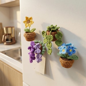 May include: Four crochet plant magnets in various colours. A yellow sunflower, a green trailing plant, a purple wisteria, and a blue flower, each in a brown pot. The magnets are attached to a white fridge.