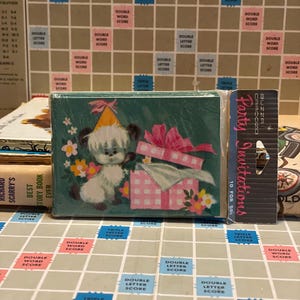 May include: A stack of party invitations with a cartoon puppy wearing a party hat and a pink gift box on the front. The invitations are packaged in a clear plastic wrap. A vintage Scrabble board is in the background.