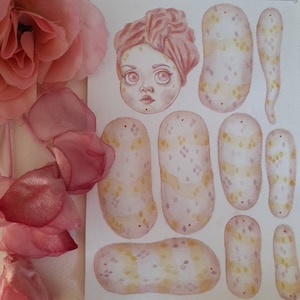 Pode incluir: Uma boneca de papel com um turbante rosa e um vestido estampado em rosa e amarelo. A boneca é composta por peças separadas que podem ser recortadas e montadas.