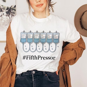 May include: White t-shirt featuring a medical-themed graphic. The design includes six IV bags with labels like "LEVO" and "EPI", connected by tubes with water droplets. The text "#FifthPressor" is printed below the bags.