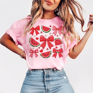 Pode incluir: Camiseta rosa com estampa de melancia e la&ccedil;os. As fatias de melancia s&atilde;o vermelhas e verdes com sementes pretas. Os la&ccedil;os s&atilde;o vermelhos com bolinhas brancas e vermelhos e brancos xadrez.