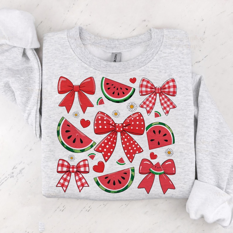 Pode incluir: Uma camisola cinzenta com um design de melancia e la&ccedil;os. A melancia &eacute; vermelha e verde com sementes pretas. Os la&ccedil;os s&atilde;o vermelhos e brancos com bolinhas brancas.