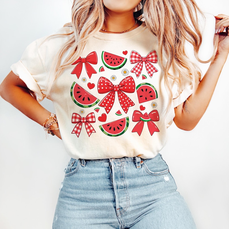 Pode incluir: Uma camiseta branca com um design de melancia e la&ccedil;o vermelho e branco. A camiseta tem gola redonda e mangas curtas.