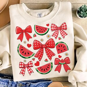 Pode incluir: Uma camisola de cor creme com um padr&atilde;o de melancia vermelha e branca e la&ccedil;os. Os la&ccedil;os s&atilde;o de v&aacute;rios estilos, incluindo xadrez, bolinhas e vermelho s&oacute;lido.