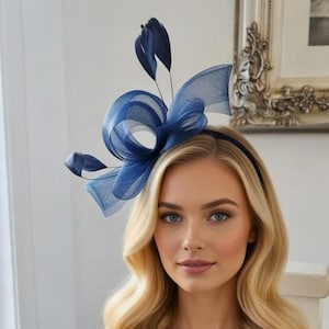 May include: A woman wearing a navy blue headband with a large bow and feather detailing. The bow is made of a sheer fabric. She is wearing a navy blue dress with lace detailing. Her blonde hair is styled in loose waves.