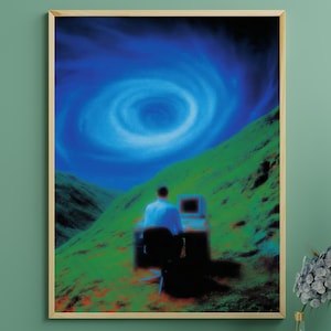 Puede incluir: Una impresión artística enmarcada que presenta un paisaje surrealista. Una persona está sentada frente a una computadora en una ladera verde, mirando hacia un vórtice azul arremolinado en el cielo. La obra de arte tiene una calidad retro y onírica.