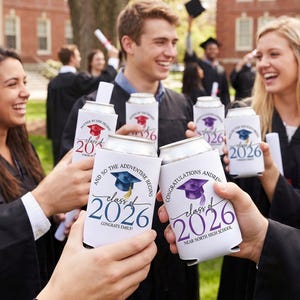 Puede incluir: Celebración de graduación con personas sosteniendo fundas blancas para latas. Las fundas muestran "Class of 2026" y diseños de birretes. También se ve el texto "And so the adventure begins".