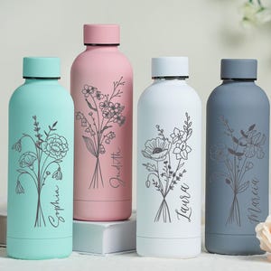 Può includere: Quattro borracce isolate in colori pastello: verde acqua, rosa, bianco e grigio. Ogni bottiglia presenta un design floreale e un nome in corsivo. Le bottiglie hanno tappi neri e sono disposte su una superficie bianca.
