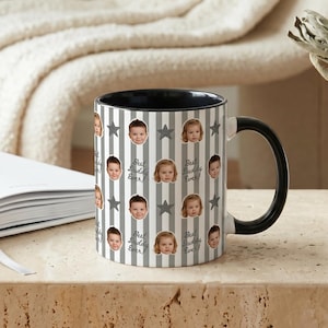 May include: A ceramic mug with a black handle and interior. The mug features a pattern of baby faces, gray stars, and vertical gray and white stripes. The text "Best Daddy Ever!" is also printed on the mug.