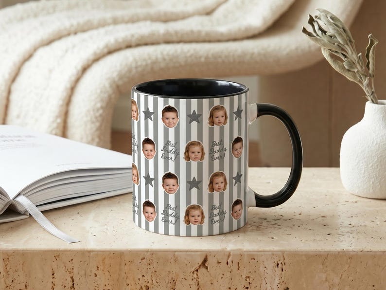 May include: A ceramic mug with a black handle and interior. The mug features a pattern of baby faces, gray stars, and vertical gray and white stripes. The text "Best Daddy Ever!" is also printed on the mug.