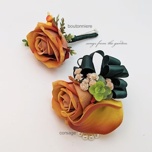 May include: A set of two floral arrangements featuring orange roses and calla lilies with green accents. The smaller arrangement is labeled "boutonniere" and the larger arrangement is labeled "corsage". The text "songs from the garden" is also included in the image.