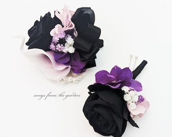 May include: Two floral arrangements. One is a wrist corsage with black, purple, and pink flowers, a black bow, and a pearl bracelet. The other is a boutonniere with a black rose, purple flowers, and white accents. The text "songs from the garden" is visible.