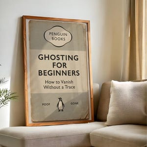May include: A framed print of a book cover titled "Ghosting for Beginners" by Penguin Books. The cover has an aged appearance, a penguin illustration, and the words "Poof" and "Gone". The frame is wooden.