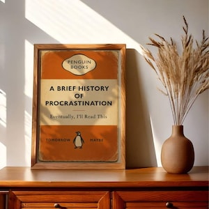 以下が含まれることがあります： ペンギンブックスの「A Brief History of Procrastination」というタイトルの本の表紙の額装されたプリント。表紙はオレンジとクリーム色で、ペンギンのイラストが描かれています。テキストは「Eventually, I'll Read This」と「Tomorrow Maybe」と書かれています。