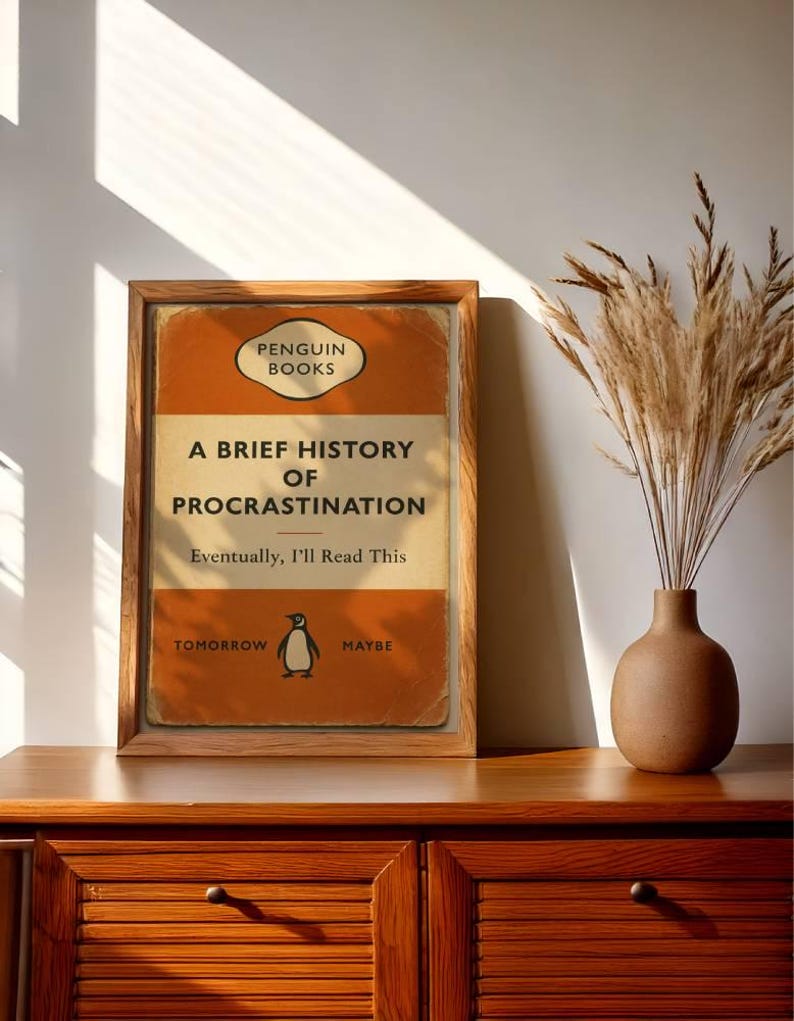 以下が含まれることがあります： ペンギンブックスの「A Brief History of Procrastination」というタイトルの本の表紙の額装されたプリント。表紙はオレンジとクリーム色で、ペンギンのイラストが描かれています。テキストは「Eventually, I'll Read This」と「Tomorrow Maybe」と書かれています。