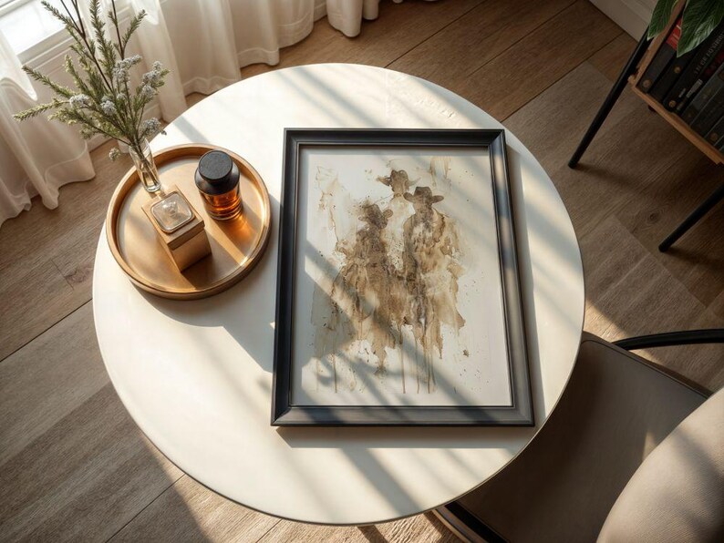 May include: A framed artwork with a watercolour painting of three figures wearing hats. The artwork is in a black frame and rests on a white round table. A gold tray with a small vase and a dark bottle sits on the table.