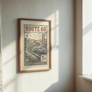 May include: Framed vintage-style Route 66 print. The artwork features a winding road, a classic car, and the text "Route 66" in a retro design. The print is in a wooden frame and is displayed on a white wall.