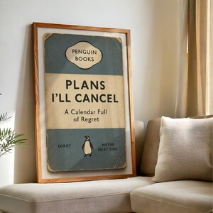 May include: A framed print with a vintage book cover design. The text reads "PLANS I'LL CANCEL" with "Penguin Books" at the top. A penguin illustration is featured, with the phrases "Sorry" and "Maybe Next Time".