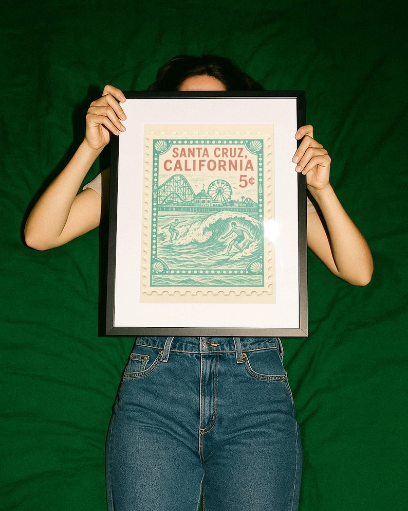 Może przedstawiać: Oprawiony wydruk z projektem znaczka pocztowego w stylu vintage. Znaczek głosi "Santa Cruz, California" i przedstawia surfer&oacute;w, kolejkę g&oacute;rską i diabelski młyn. Wydruk jest trzymany na zielonym tle.
