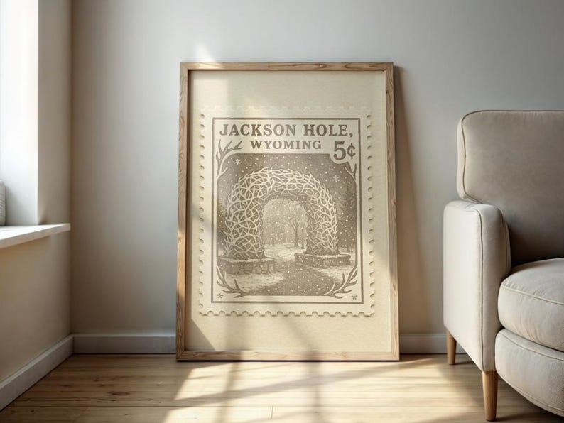 May include: A framed print featuring a vintage-style illustration of an archway in Jackson Hole, Wyoming, resembling a postage stamp. The artwork is in sepia tones and includes the text "Jackson Hole, Wyoming 5&cent;". The print is displayed against a neutral wall.