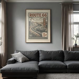 May include: A framed Route 66 poster with a vintage design, featuring a car on a winding road, a motel, and the text "Route 66". The poster is displayed above a dark gray sectional sofa in a living room setting.