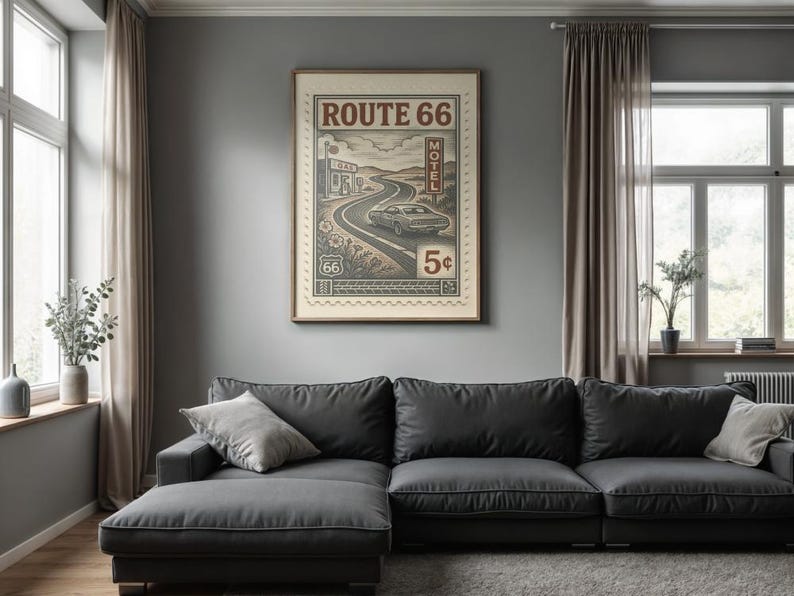 May include: A framed Route 66 poster with a vintage design, featuring a car on a winding road, a motel, and the text "Route 66". The poster is displayed above a dark gray sectional sofa in a living room setting.