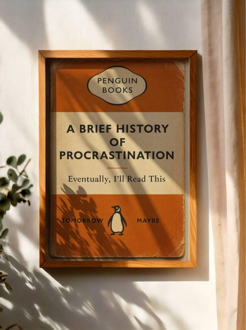 以下が含まれることがあります： 「A Brief History of Procrastination」というタイトルのペンギンブックスの書籍カバーの額装プリント。オレンジと白のカバーには、ペンギンのイラストと「Eventually, I'll Read This」と「Tomorrow Maybe」のテキストが記載されています。