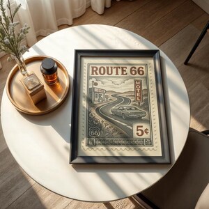 May include: Framed Route 66 print with a black border. The vintage-style artwork depicts a car driving on a winding road, with the words "Route 66" at the top. The print also includes a gas station, motel, and the number "5&cent;".