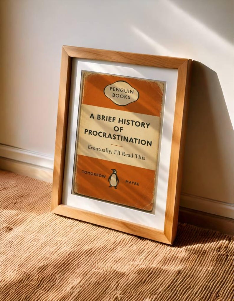 以下が含まれることがあります： ペンギンブックスの「A Brief History of Procrastination」というタイトルの本の表紙の額装プリント。表紙はオレンジとクリーム色で、ペンギンのイラストが描かれています。テキストは「Eventually, I'll Read This」と書かれています。
