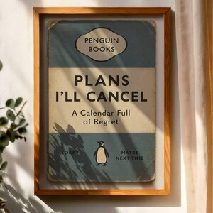 May include: A framed print of a book cover with the title "PLANS I'LL CANCEL" and the Penguin Books logo. The cover is blue and beige with a penguin illustration. The text "A Calendar Full of Regret" is also visible.