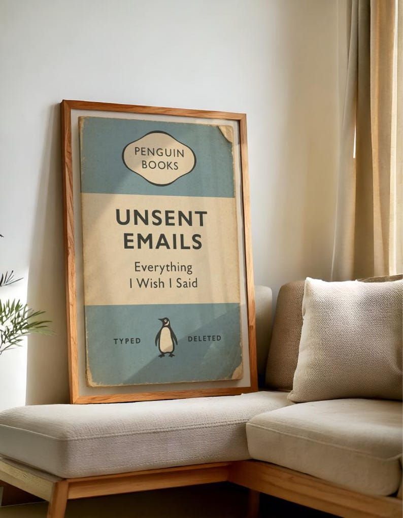 May include: A framed print resembling a vintage book cover. The design features the text "UNSENT EMAILS" and "Everything I Wish I Said" with a penguin illustration. The frame is made of wood.