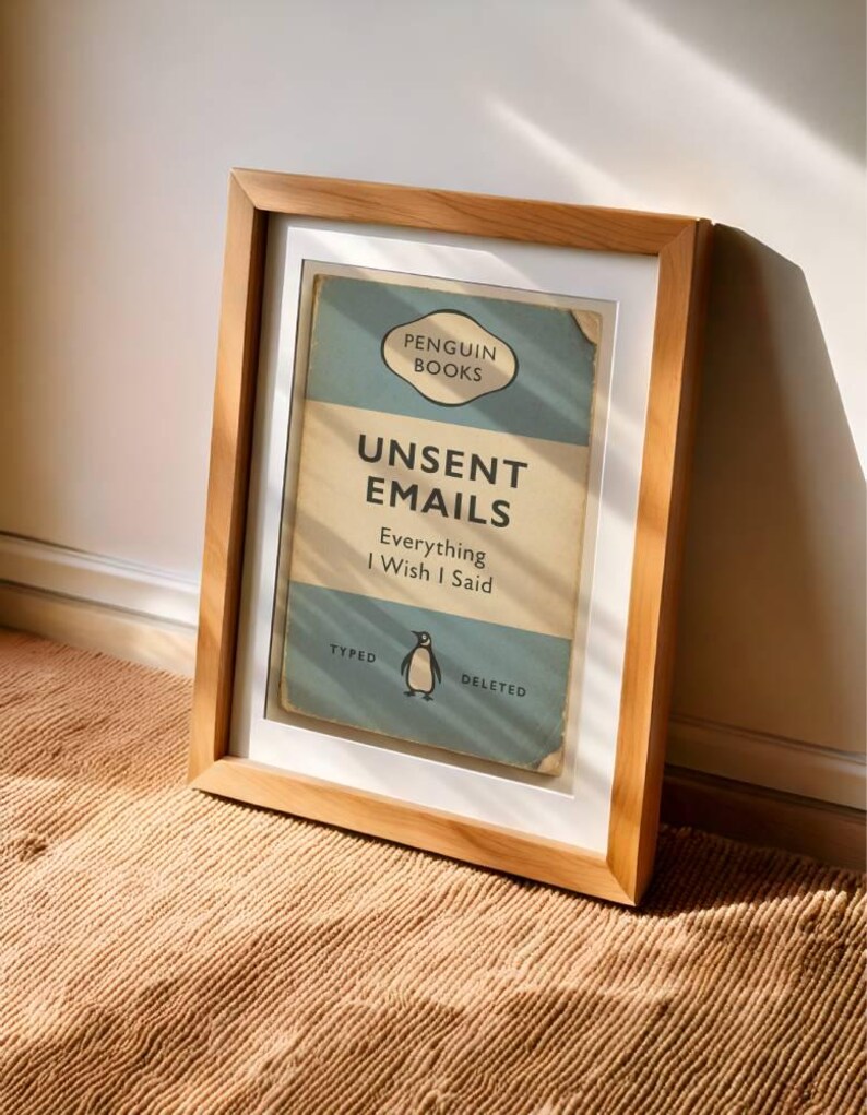 May include: A framed print of a book cover titled "Unsent Emails" by Penguin Books. The design features a vintage aesthetic with a light blue and beige color scheme. The frame is made of light-colored wood.