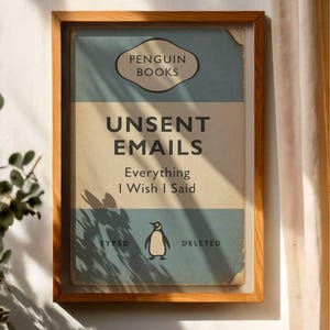 May include: Framed print with a vintage book cover design. The text reads "UNSENT EMAILS Everything I Wish I Said" with a penguin illustration. The frame is made of light brown wood.