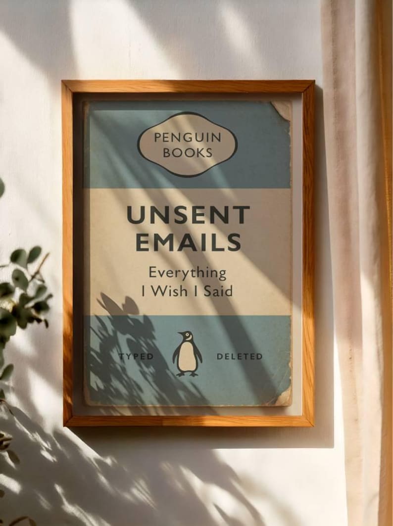 May include: Framed print with a vintage book cover design. The text reads "UNSENT EMAILS Everything I Wish I Said" with a penguin illustration. The frame is made of light brown wood.