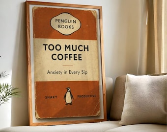 Peut inclure: Impression encadrée avec un design de couverture de livre vintage. La couverture est orange et crème, avec le texte "TOO MUCH COFFEE" et "Anxiety in Every Sip". Une illustration de pingouin est centrée en dessous. Le cadre est en bois clair.