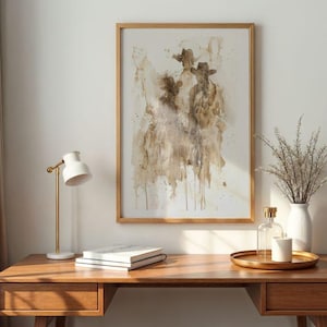 May include: Abstract art print in a wooden frame, featuring a brown and beige watercolour design of figures wearing hats. The print is above a wooden desk with a white lamp, books, and decorative items.
