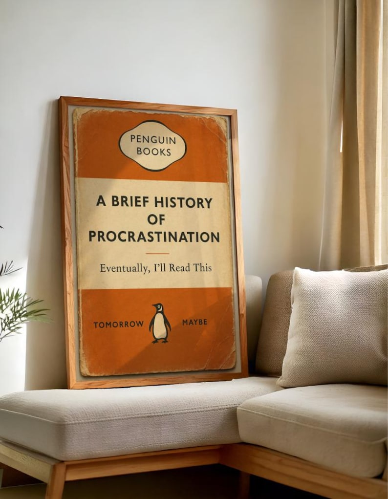 以下が含まれることがあります： ペンギンブックスの「A Brief History of Procrastination」というタイトルの本の表紙の額入りプリント。表紙はオレンジとクリーム色で、ペンギンのイラストが描かれています。テキストは「Eventually, I'll Read This」と「Tomorrow Maybe」と書かれています。
