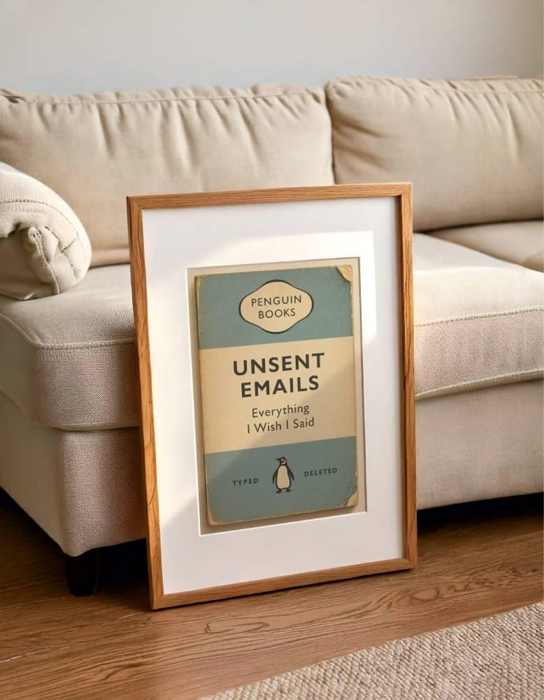 May include: Framed print featuring a vintage Penguin Books cover design. The cover is light blue and tan, with the title "Unsent Emails: Everything I Wish I Said." The frame is a light brown wood, and the print is matted in white.