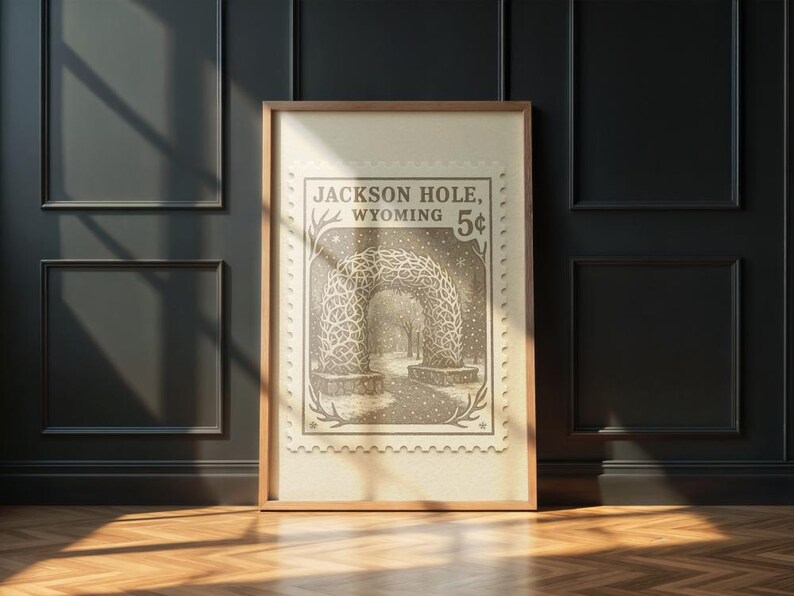 May include: Framed print of a vintage postage stamp design featuring an archway in Jackson Hole, Wyoming. The stamp is in sepia tones with the text "Jackson Hole, Wyoming 5&cent;". The print is in a wooden frame.