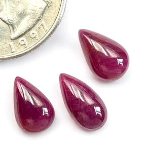 May include: Three teardrop-shaped, polished ruby gemstones. The gems are a deep, rich red color with a glossy surface. A quarter coin is in the background, showing the year 1997.