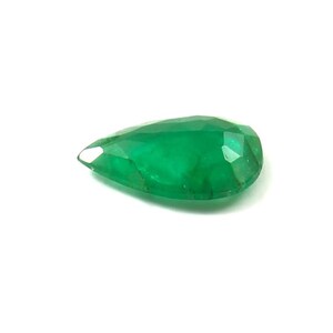 May include: A faceted, pear-shaped emerald gemstone. The gem is a vibrant green color and has a polished surface. The cut of the stone reveals multiple facets, enhancing its brilliance. The gemstone is set against a white background.