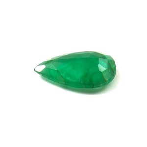 May include: A faceted, pear-shaped emerald gemstone. The gem is a vibrant green color and has a polished surface. The cut of the stone reveals multiple facets, enhancing its brilliance. The gemstone is set against a white background.