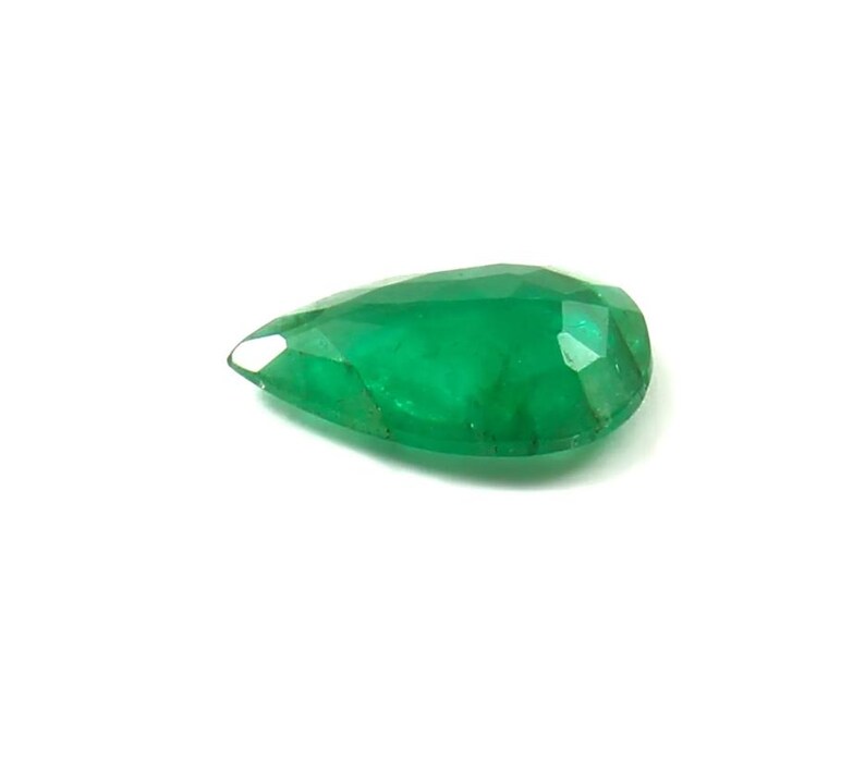 May include: A faceted, pear-shaped emerald gemstone. The gem is a vibrant green color and has a polished surface. The cut of the stone reveals multiple facets, enhancing its brilliance. The gemstone is set against a white background.
