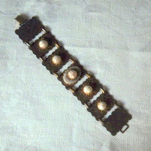 May include: A brown metal bracelet with five decorative round white and gold accents.