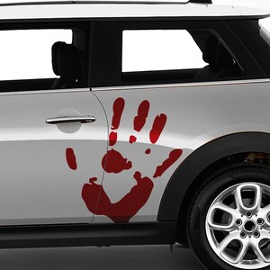 Op de afbeelding: Een zilverkleurige autodeur met een grote, donkerrode handafdruksticker die over het deurpaneel en het achterpaneel is aangebracht. De sticker bootst de vorm van een menselijke hand na met duidelijke vingers en een handpalm bij de klink.