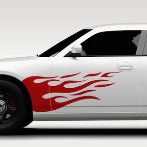 Könnte beinhalten: Ein weißes Auto mit einem großen, roten, flammenförmigen Aufkleber auf dem vorderen Kotflügel und der Türverkleidung. Das Grafikdesign besteht aus stilisierten, länglichen Flammenzungen, die sich horizontal über die Fahrzeugseite erstrecken.