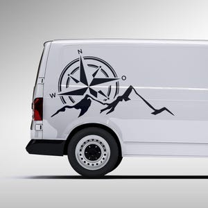Può includere: Furgone bianco con un adesivo nero a forma di bussola e catena montuosa. La bussola presenta punti direzionali e un design a stella. La catena montuosa è raffigurata in uno stile minimalista.