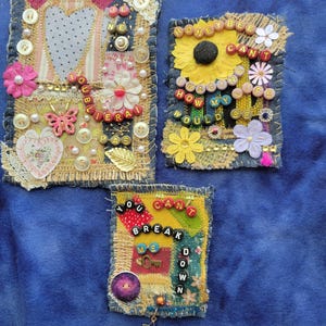 May include: Three handmade fabric art pieces with denim and burlap textures. Embellishments include buttons, beads, and floral accents. One piece features the text "YOU CAN'T BREAK ME DOWN." Another says "HONEY BEE CAN'T IMAGINE HOW MY LIFE WOULD BE."