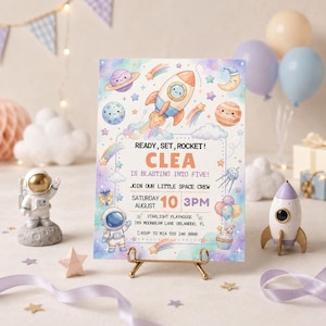Puede incluir: Una tarjeta de invitación rectangular con temática espacial que muestra un cohete, planetas, estrellas y un astronauta. El texto dice: READY, SET, ROCKET! CLEA IS BLASTING INTO FIVE! JOIN OUR LITTLE SPACE CREW SATURDAY AUGUST 10 3PM STARLIGHT PLAYHOUSE.