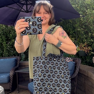 May include: A matching set of accessories featuring a repeating black cat face pattern on a blue background. The set includes a wallet and a tote bag. The tote bag has a long strap and is made of a sturdy fabric.